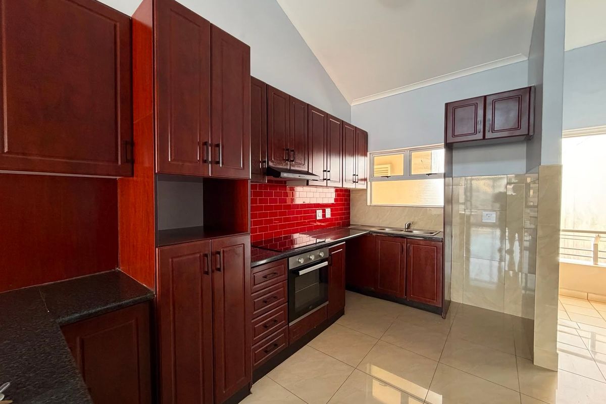 A clean, modern kitchen featuring dark wood cabinetry, granite countertops, a red tiled backsplash, and built-in appliances, offering a functional and well-maintained cooking space.