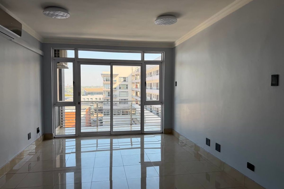 A bright, empty living room featuring polished tile floors, cove ceiling molding, and a large sliding glass door leading to a balcony.