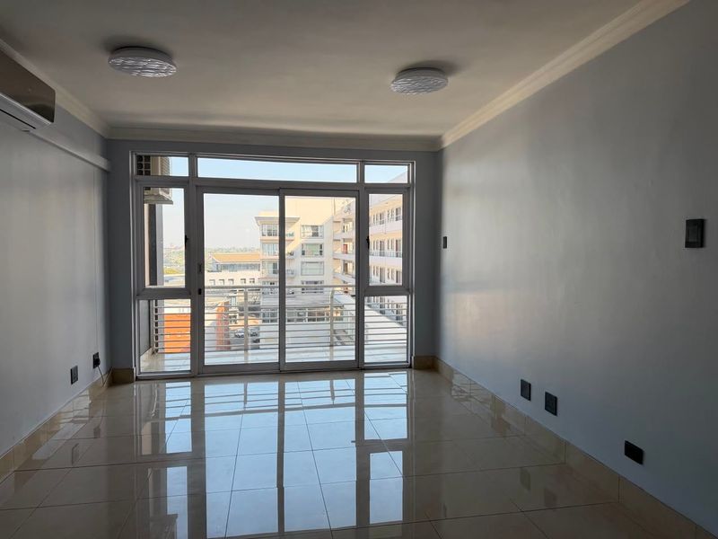 A bright, empty living room featuring polished tile floors, cove ceiling molding, and a large sliding glass door leading to a balcony.
