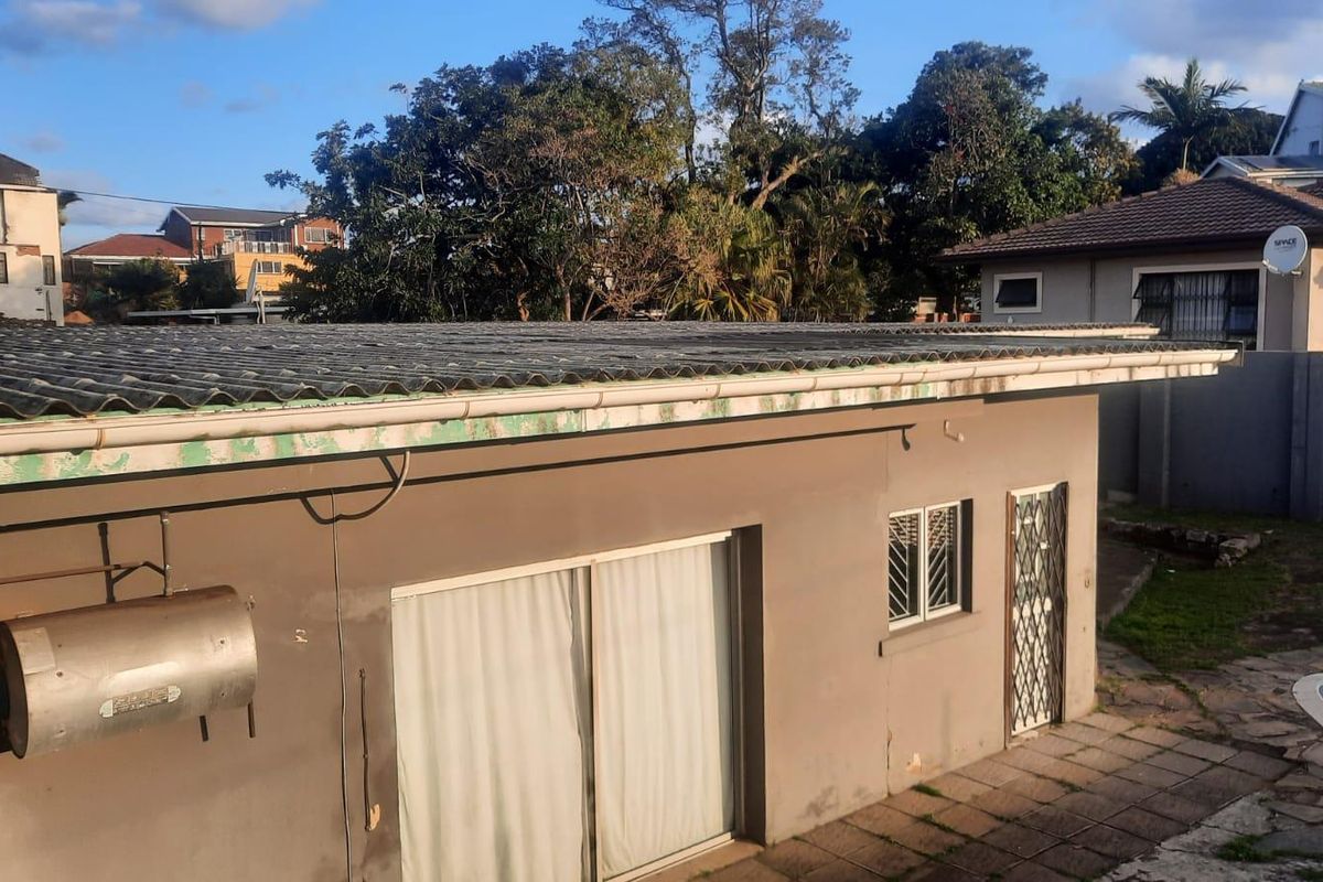 Rear exterior view of the property featuring a corrugated roof, external geyser, sliding door access, and paved patio area adjacent to a swimming pool.