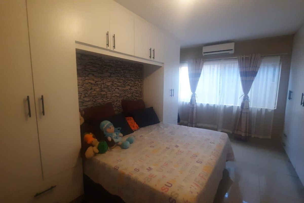 A well-lit bedroom featuring extensive built-in cupboard storage, tiled flooring, and a wall-mounted air conditioning unit.