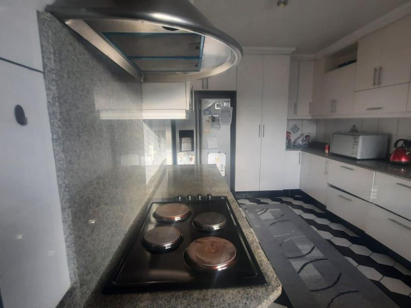 A functional kitchen featuring granite countertops, built-in cabinetry, an electric hob with extractor fan, and distinctive patterned floor tiling.