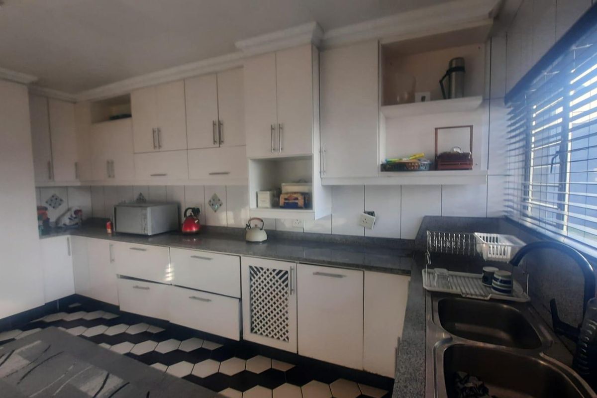 A functional kitchen featuring white cabinetry, stone countertops, a double bowl sink, and a distinctive monochrome geometric tiled floor.