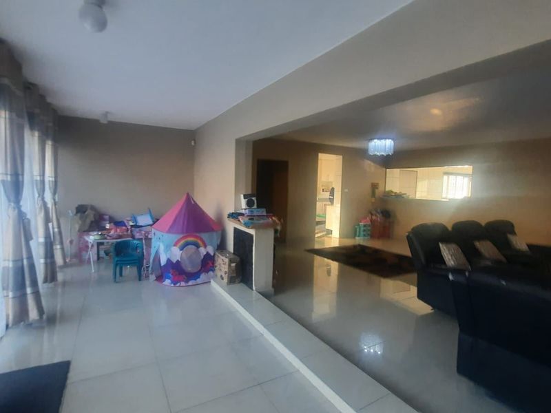 Spacious open-plan living area featuring tiled flooring, neutral walls, and a convenient pass-through window connecting to the kitchen space.
