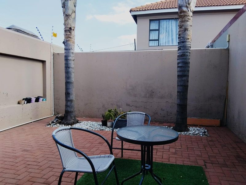 A private rear courtyard featuring paved flooring, boundary walls with electric fencing, and established palm trees, offering a low-maintenance outdoor space.