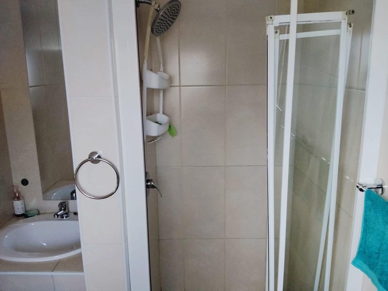A functional bathroom featuring a shower enclosure with a tiled surround, a vanity basin with a mixer tap, and wall-mounted towel fixtures.