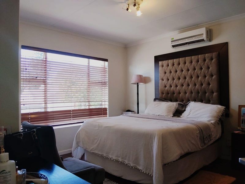 A well-maintained bedroom featuring a split-system air conditioner, large window with venetian blinds, and neutral wall finishes.