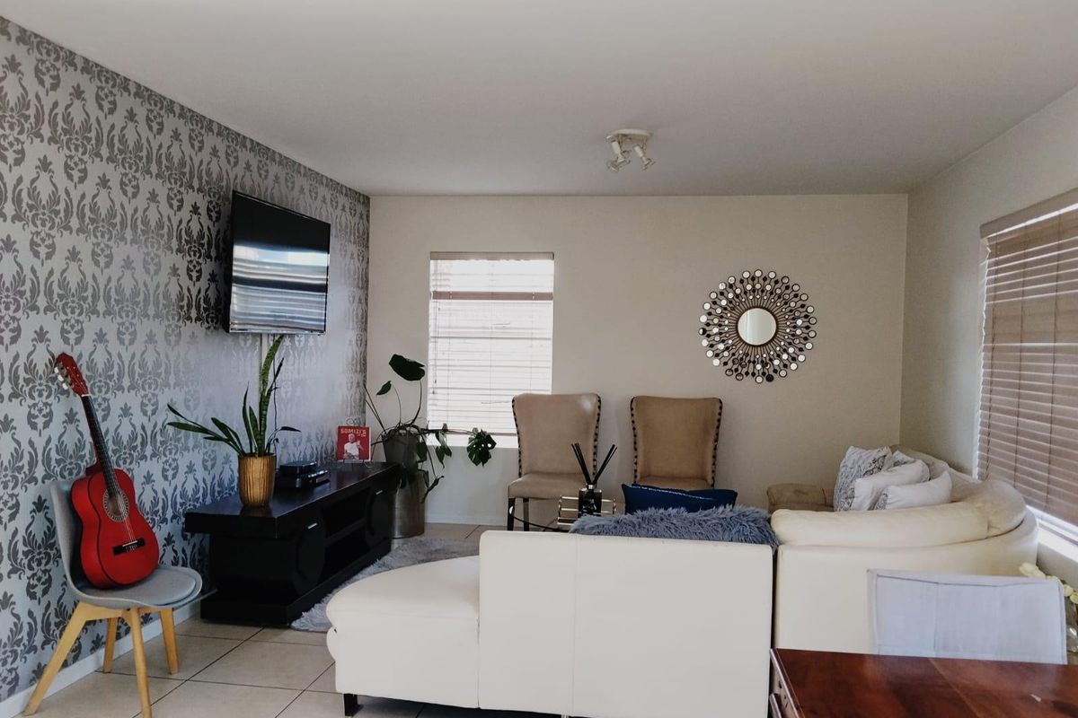 A living room featuring tiled flooring, venetian blinds, and a decorative feature wallpaper wall.