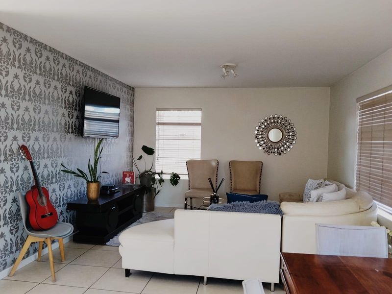 A living room featuring tiled flooring, venetian blinds, and a decorative feature wallpaper wall.