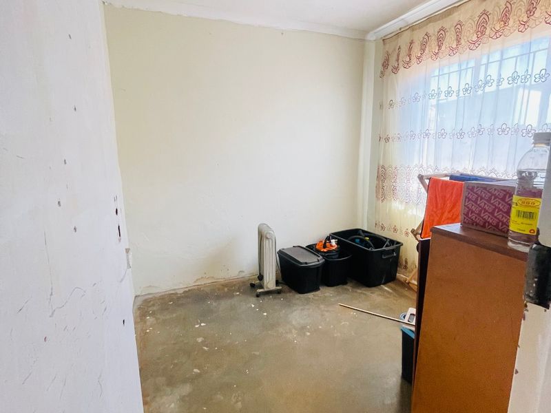An empty bedroom space featuring a window with security bars, requiring floor and wall finishing to restore its condition.