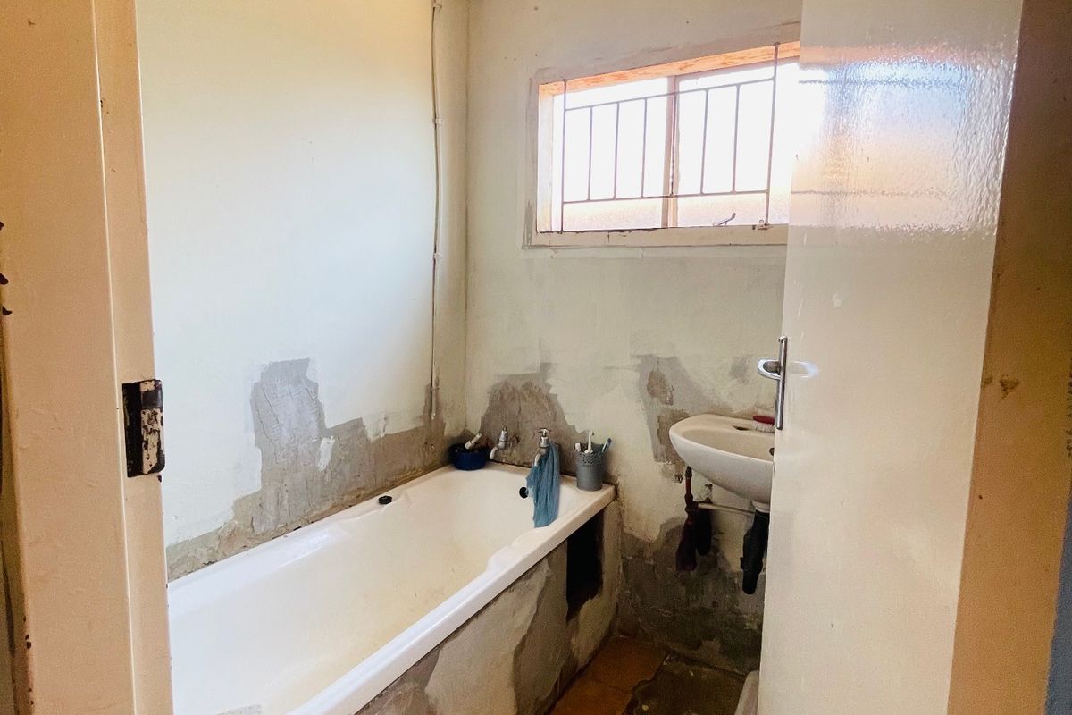 A small bathroom in need of renovation, featuring a bathtub, wall-mounted basin, and tiled flooring with significant wear to the wall and ceiling finishes.