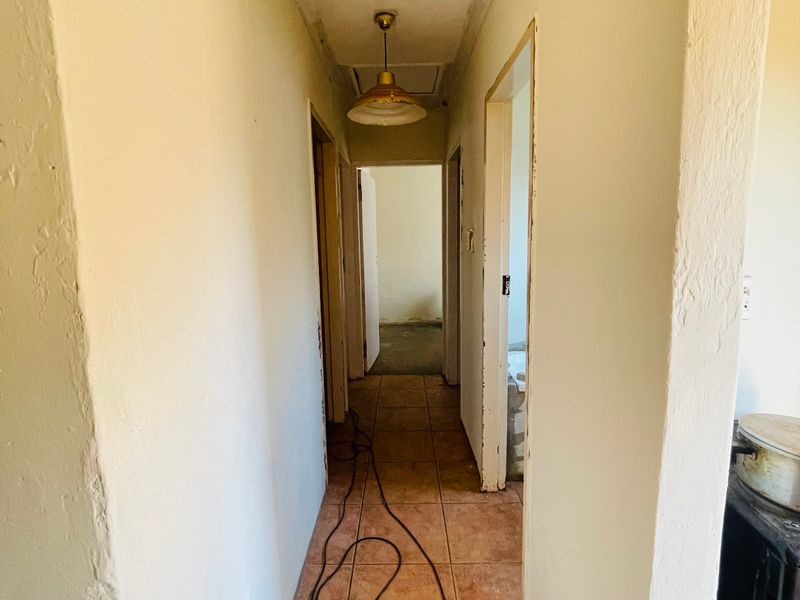A narrow residential hallway featuring tiled flooring, a central ceiling light, and access to a loft space, requiring cosmetic updates to finishes.