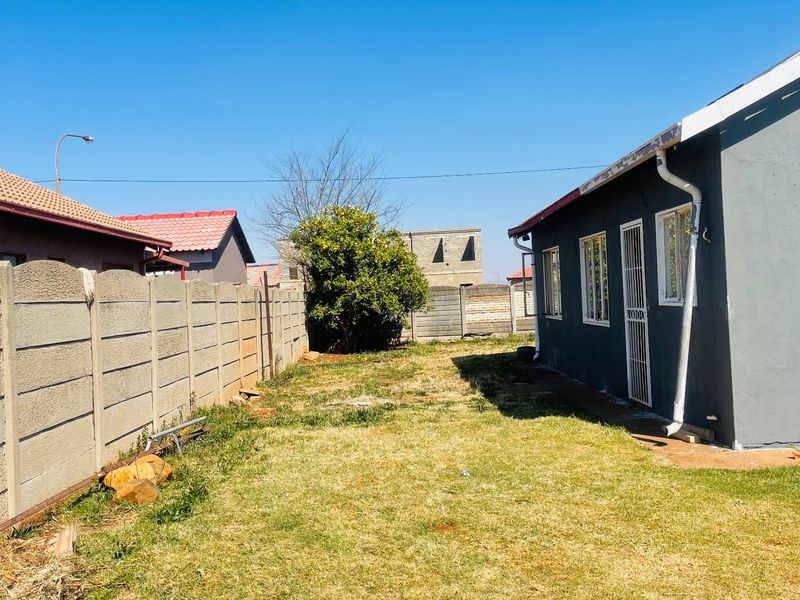 A rear garden area featuring a lawn, enclosed by a precast concrete boundary wall, with a view of the side elevation of the house.