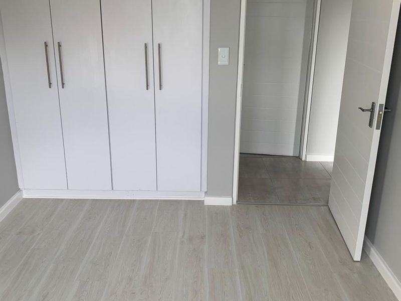 A clean, empty bedroom featuring modern laminate flooring, neutral grey walls, and built-in white cupboards with sleek handles.