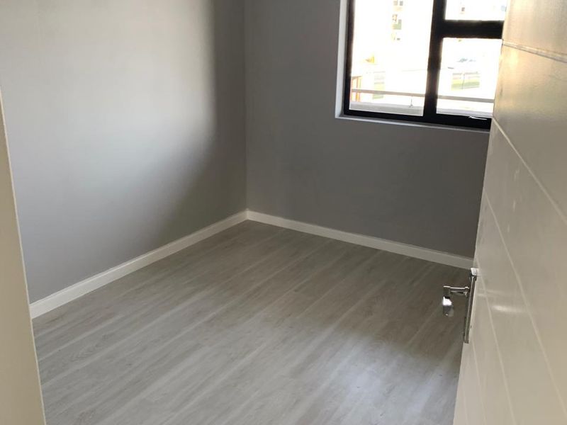 A clean, empty bedroom featuring modern grey laminate flooring, neutral walls, and a dark aluminium window frame.