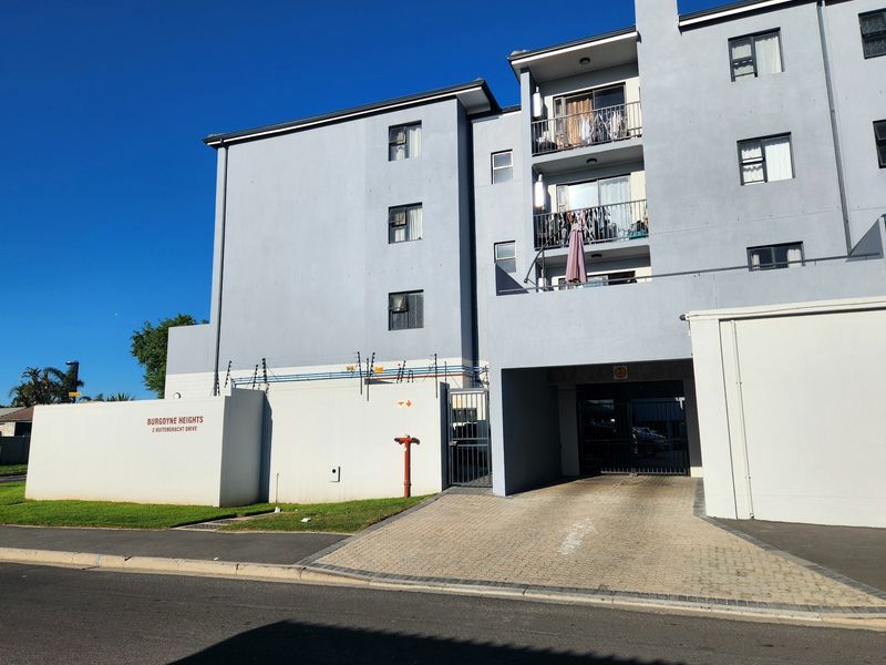 Front elevation of Burgoyne Heights apartment complex featuring a paved driveway, secure gated entrance, and multi-level balconies.