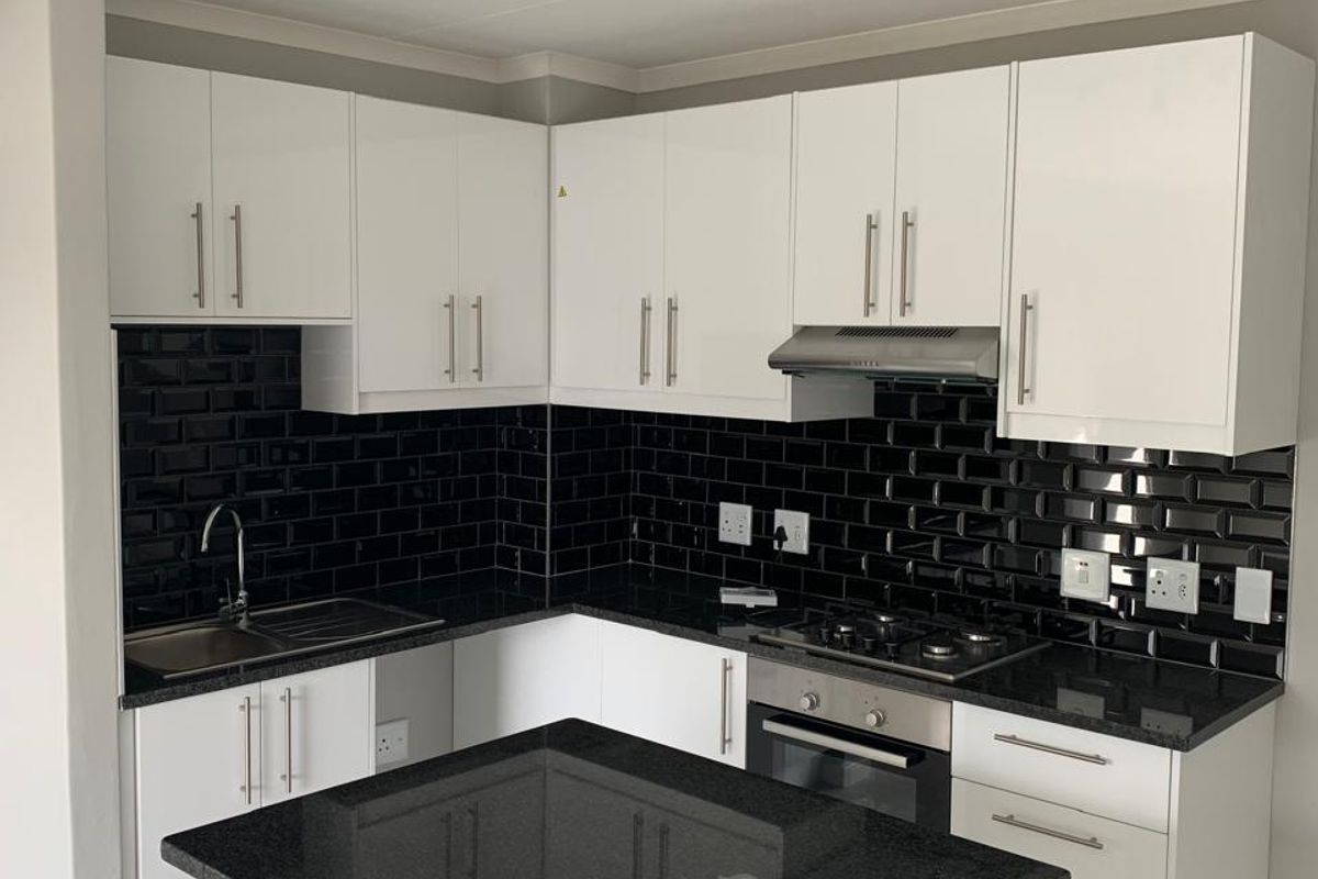 Modern kitchen featuring white cabinetry, black granite countertops, a contrasting black subway tile backsplash, built-in oven, gas hob, and a functional kitchen island.