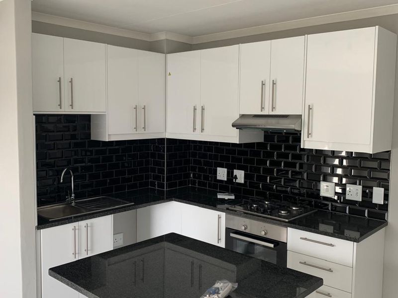 Modern kitchen featuring white cabinetry, black granite countertops, a contrasting black subway tile backsplash, built-in oven, gas hob, and a functional kitchen island.