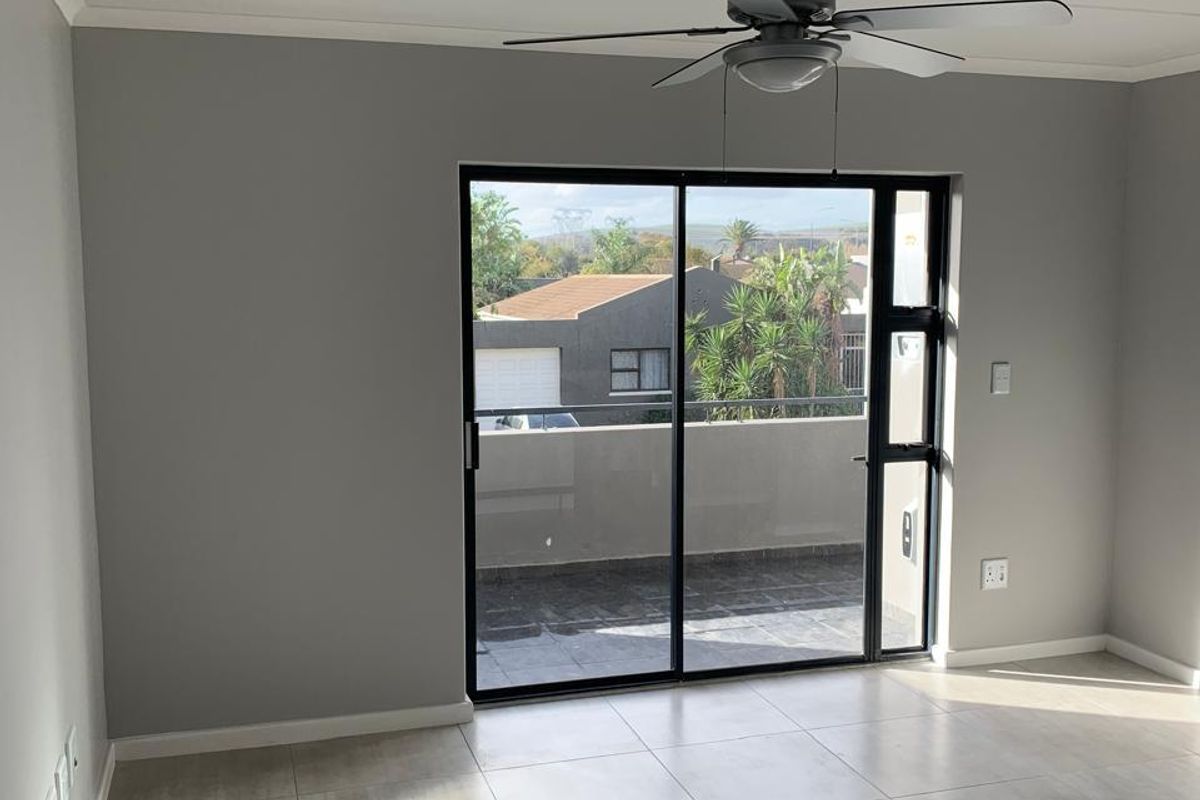 A bright, empty living room featuring neutral tiled flooring, a ceiling fan, and large sliding glass doors leading to a private balcony.