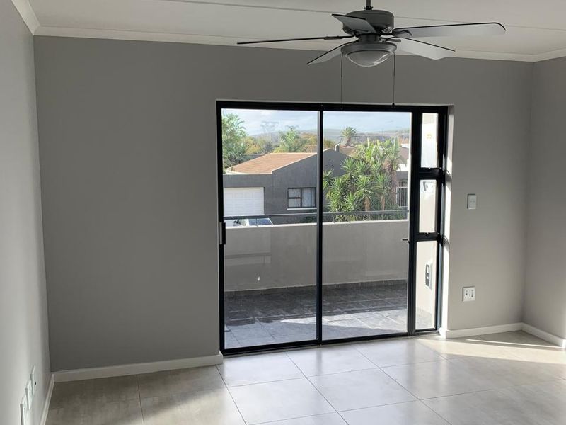A bright, empty living room featuring neutral tiled flooring, a ceiling fan, and large sliding glass doors leading to a private balcony.