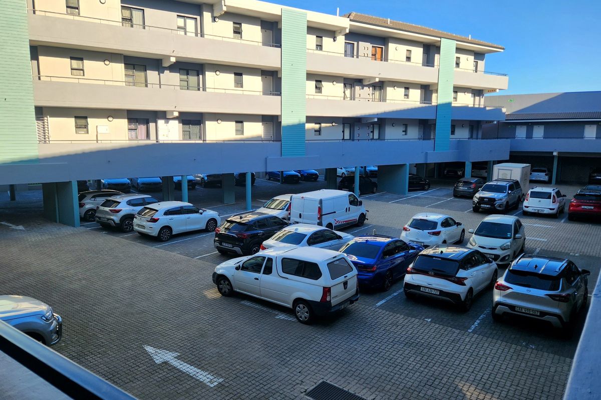 View of the apartment complex exterior featuring a paved parking area with covered bays and multi-story residential building facade.