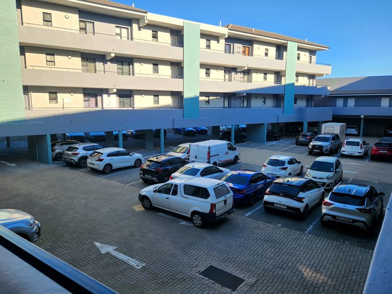 View of the apartment complex exterior featuring a paved parking area with covered bays and multi-story residential building facade.