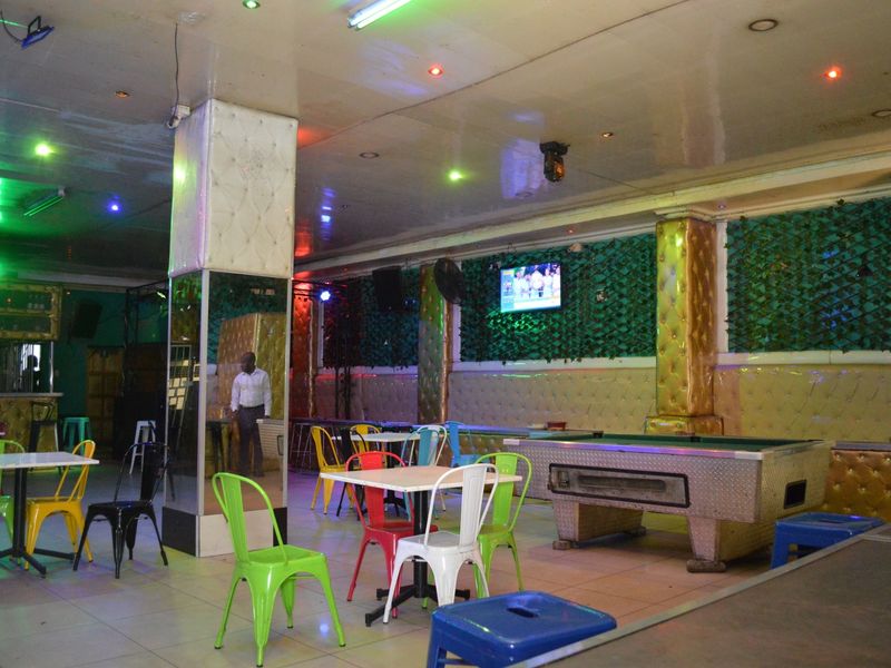 Spacious commercial bar area featuring tiled flooring, mirrored columns, and decorative upholstered wall paneling with integrated lighting.
