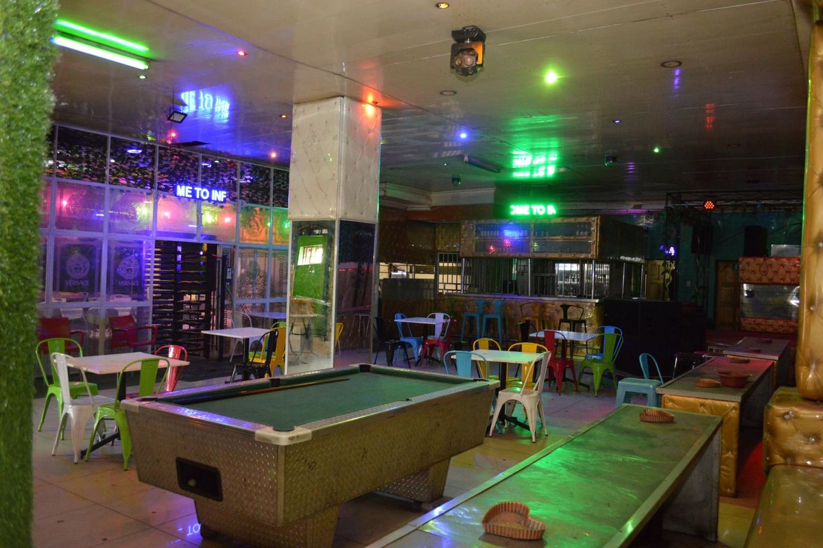 A commercial clubhouse or bar area featuring a central pool table, built-in bar counter, and integrated ceiling lighting with a tiled floor finish.