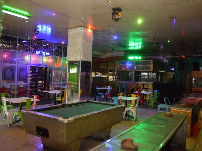 A commercial clubhouse or bar area featuring a central pool table, built-in bar counter, and integrated ceiling lighting with a tiled floor finish.