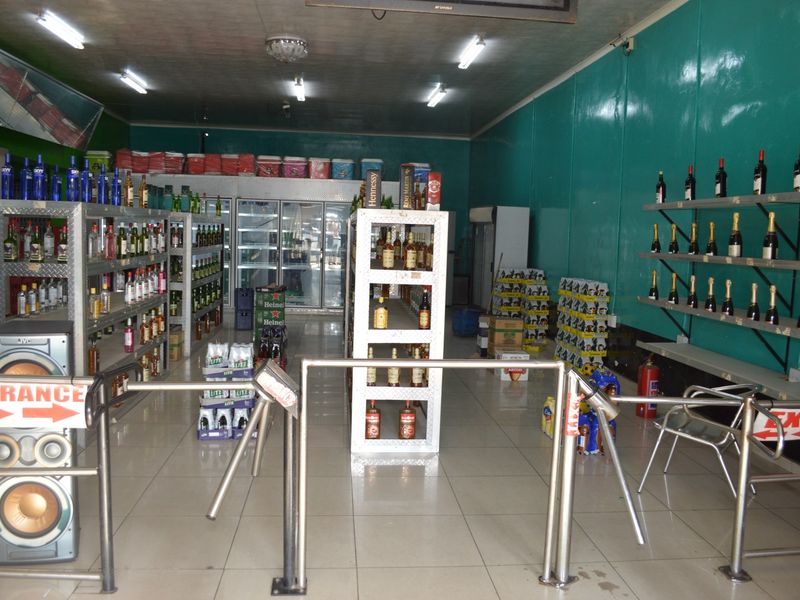 Commercial retail space featuring tiled flooring, fluorescent lighting, metal shelving units, and a turnstile entrance gate for customer flow management.