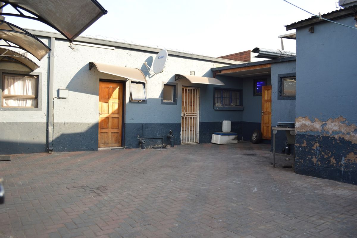 A paved rear courtyard area featuring multiple access points, security gates, and weathered exterior wall finishes requiring maintenance.