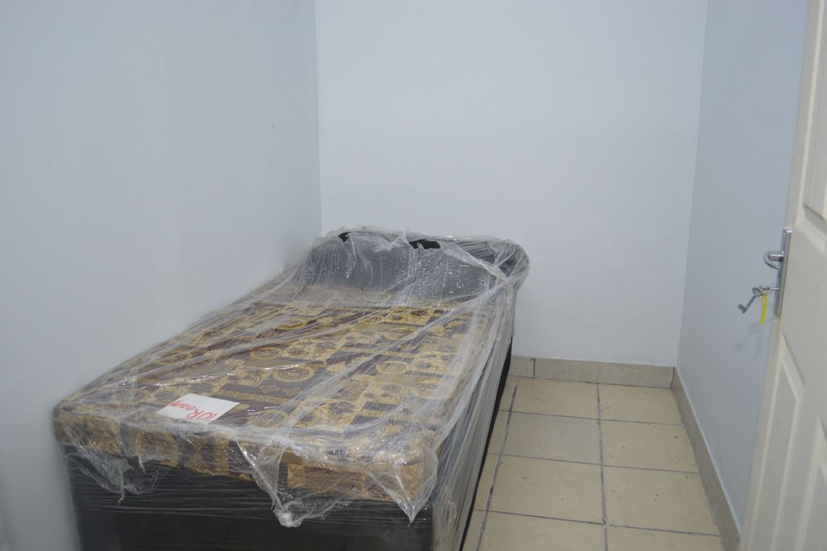 A simple, compact bedroom featuring tiled flooring and neutral wall finishes, suitable for a guest room or private office space.