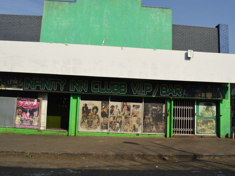 Commercial storefront featuring large display windows, security gate, and prominent signage, suitable for a bar or club venue.