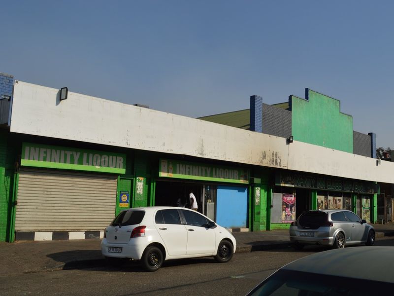 Front exterior view of a commercial building featuring roller shutter doors and prominent signage along the street frontage.