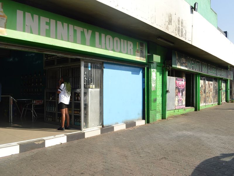 Street-level view of a commercial storefront featuring green signage, security gates, and paved sidewalk access.