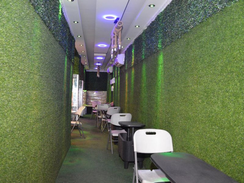 A narrow commercial space featuring artificial grass wall cladding, recessed ceiling lighting, and a split-system air conditioning unit.