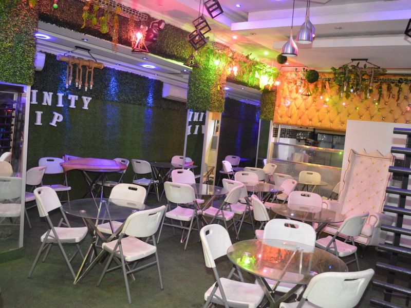 A commercial clubhouse or lounge area featuring artificial grass wall accents, decorative upholstered paneling, and integrated ceiling lighting.