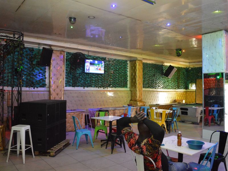 A commercial clubhouse interior featuring tiled flooring, upholstered wall paneling, integrated ceiling lighting, and wall-mounted audio equipment.