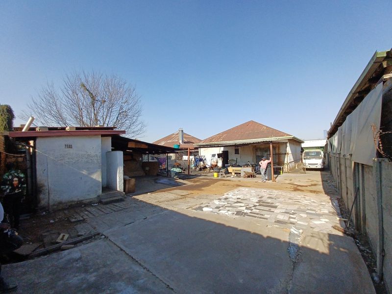 Rear exterior view of the property featuring a concrete paved yard, covered patio area, and multiple outbuildings with corrugated metal roofing.