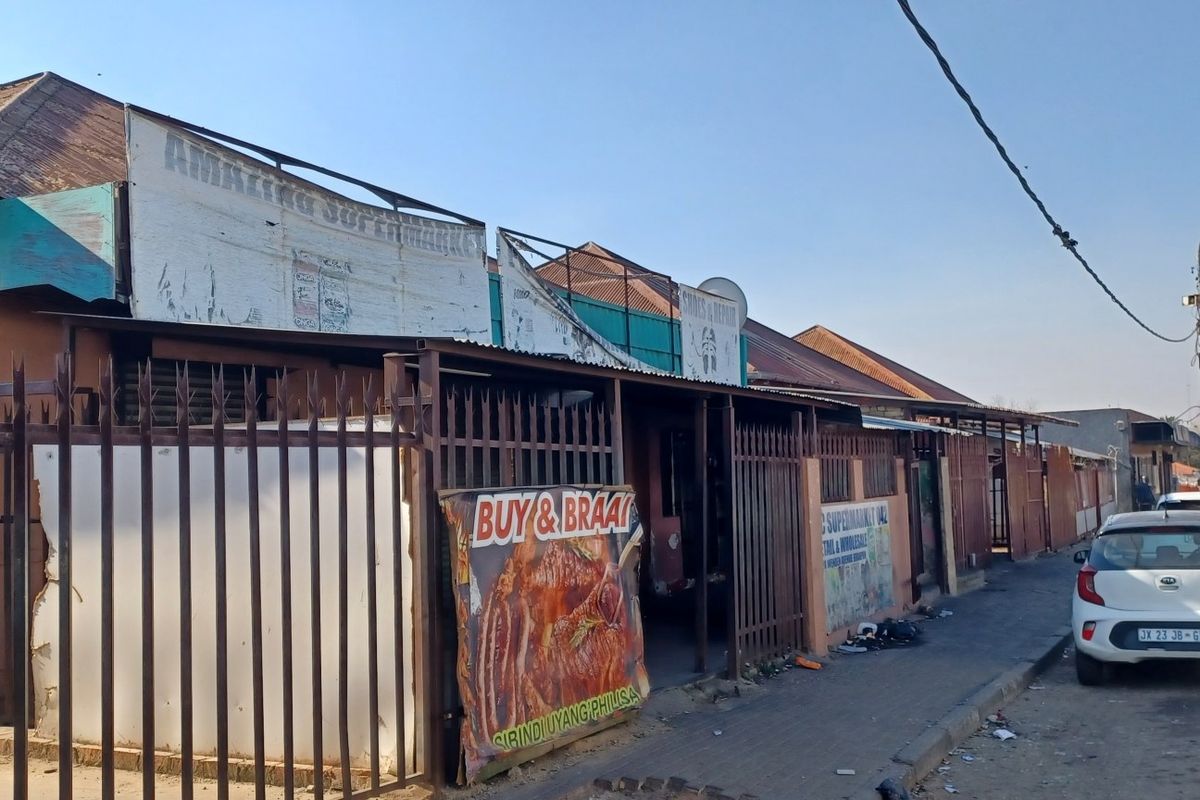 Street-level view of a commercial property featuring metal security fencing and signage along a paved sidewalk.