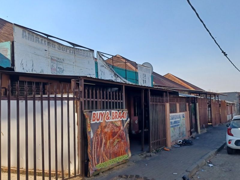 Street-level view of a commercial property featuring metal security fencing and signage along a paved sidewalk.
