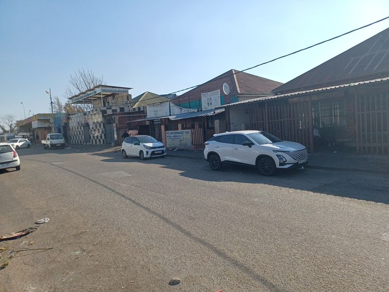A street-level view of a commercial area featuring various storefronts with security gates and tiled facades along a paved road.