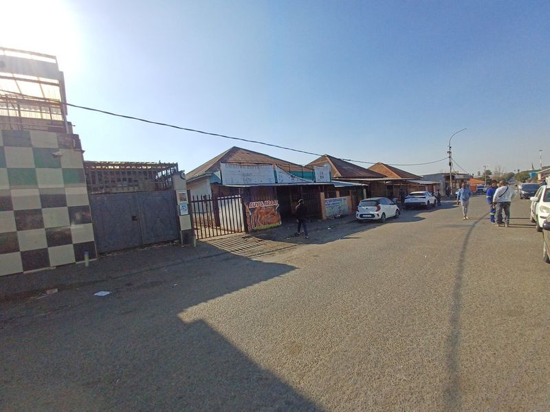 Street view of a commercial property featuring a tiled facade, metal security gates, and corrugated roofing along a paved road.