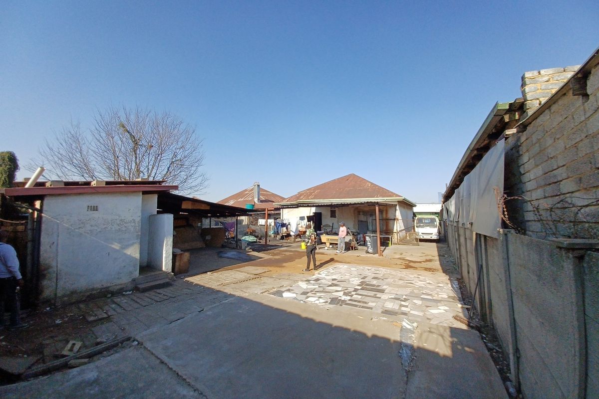 Rear exterior view of the property featuring a concrete paved yard, boundary walls, and multiple outbuildings with corrugated metal roofing.