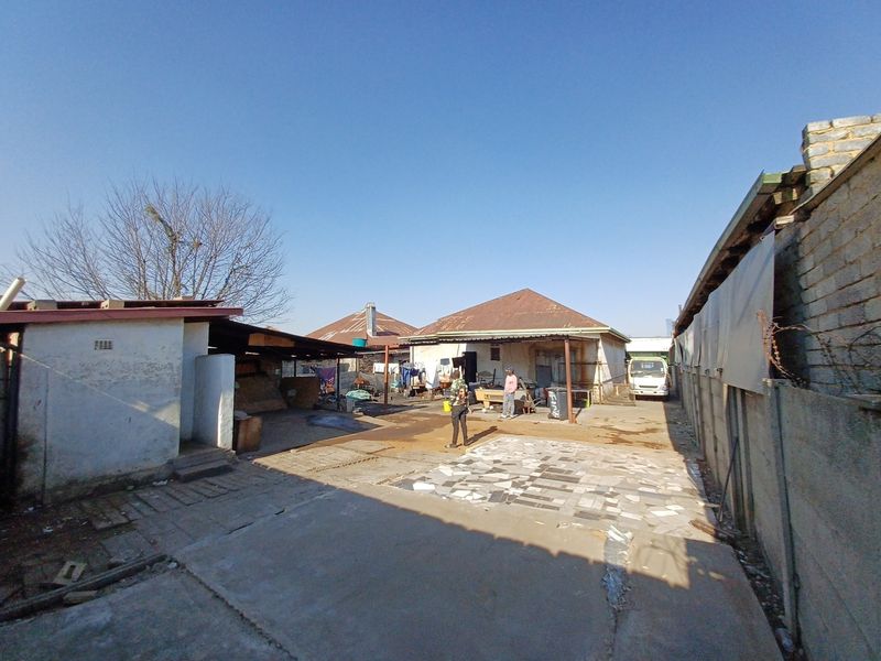 Rear exterior view of the property featuring a concrete paved yard, boundary walls, and multiple outbuildings with corrugated metal roofing.