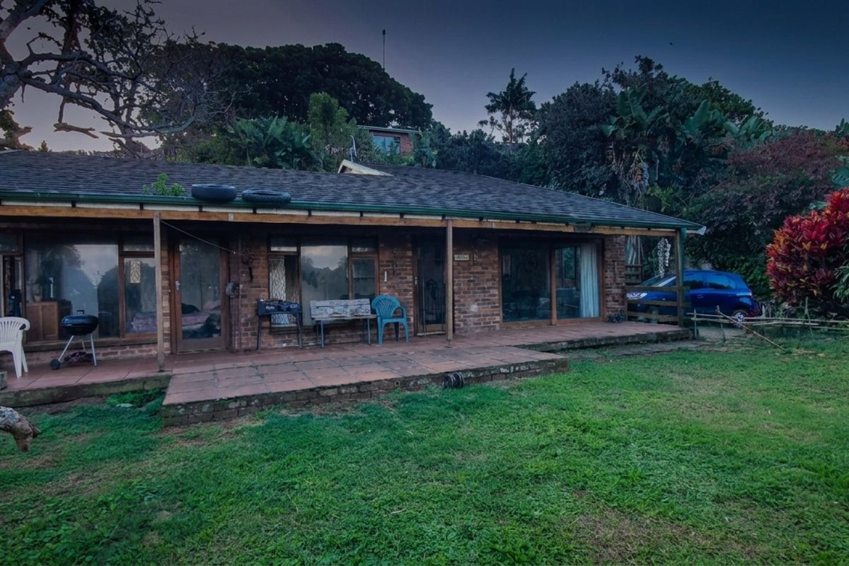 Rear view of a single-story brick house featuring a covered patio area, sliding glass doors, and a large garden space.