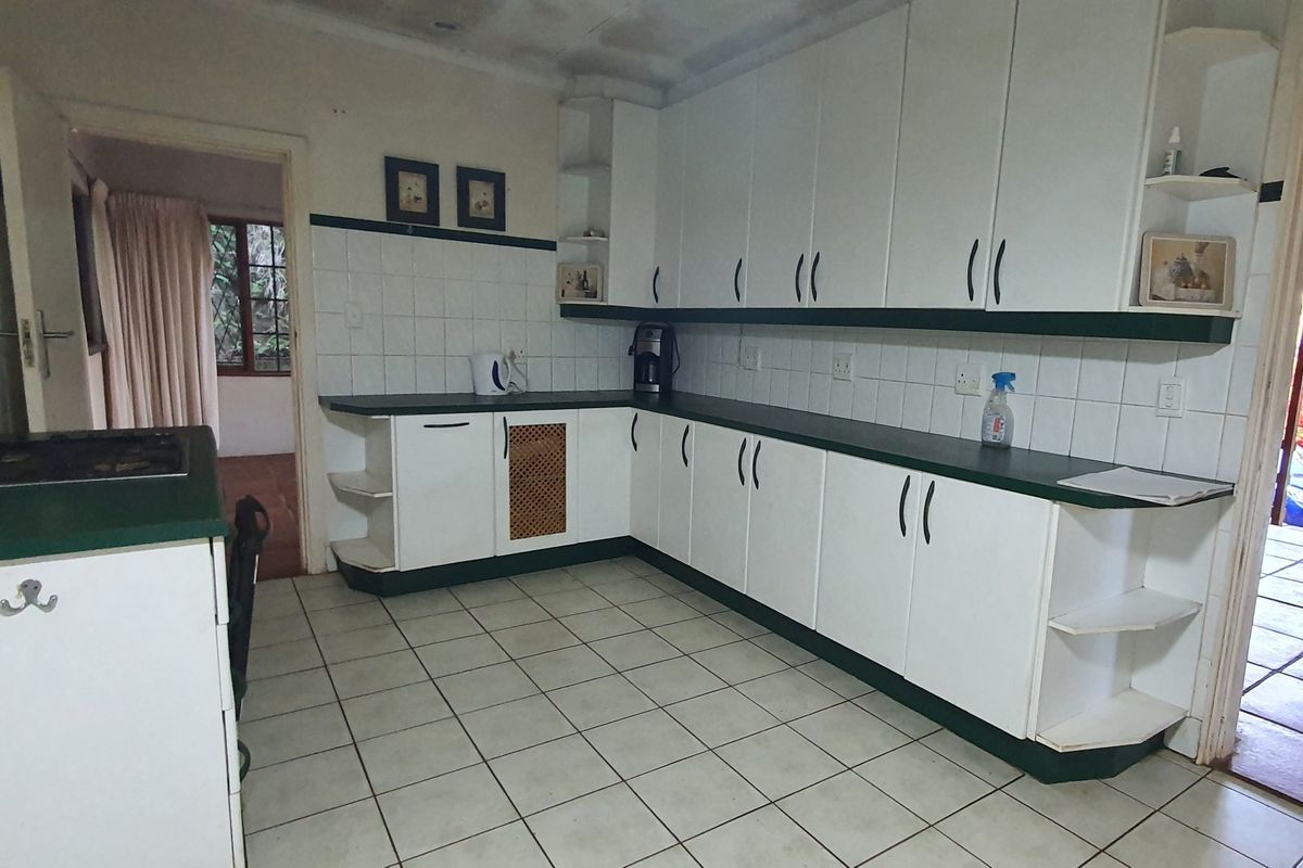 A functional kitchen featuring white cabinetry, dark laminate countertops, and tiled flooring, offering a dated aesthetic with potential for modern renovation.