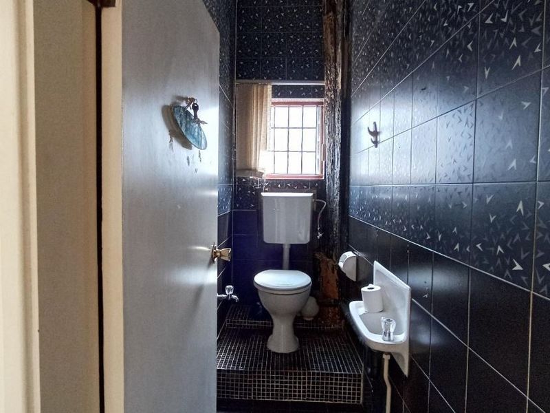 A compact bathroom featuring dark patterned wall tiles, a white toilet, and a small wall-mounted basin.