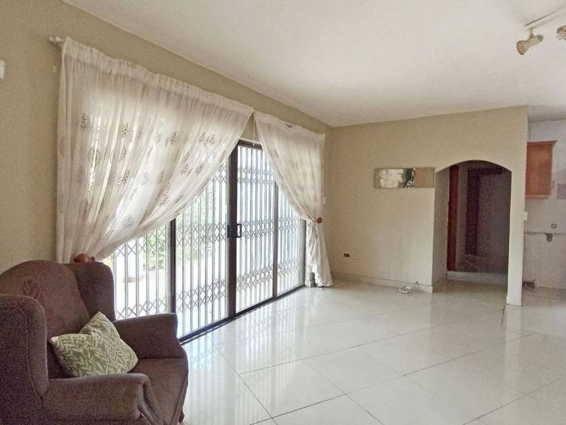 Spacious living area featuring large sliding glass doors with security gates, neutral tiled flooring, and an open-plan layout leading to adjacent spaces.