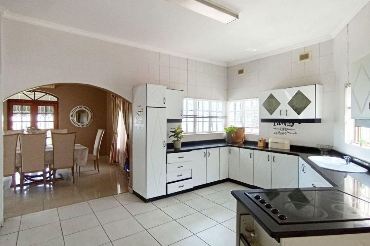 A functional kitchen featuring white cabinetry, dark countertops, and an electric hob, with an open-plan layout leading into the adjacent dining area.